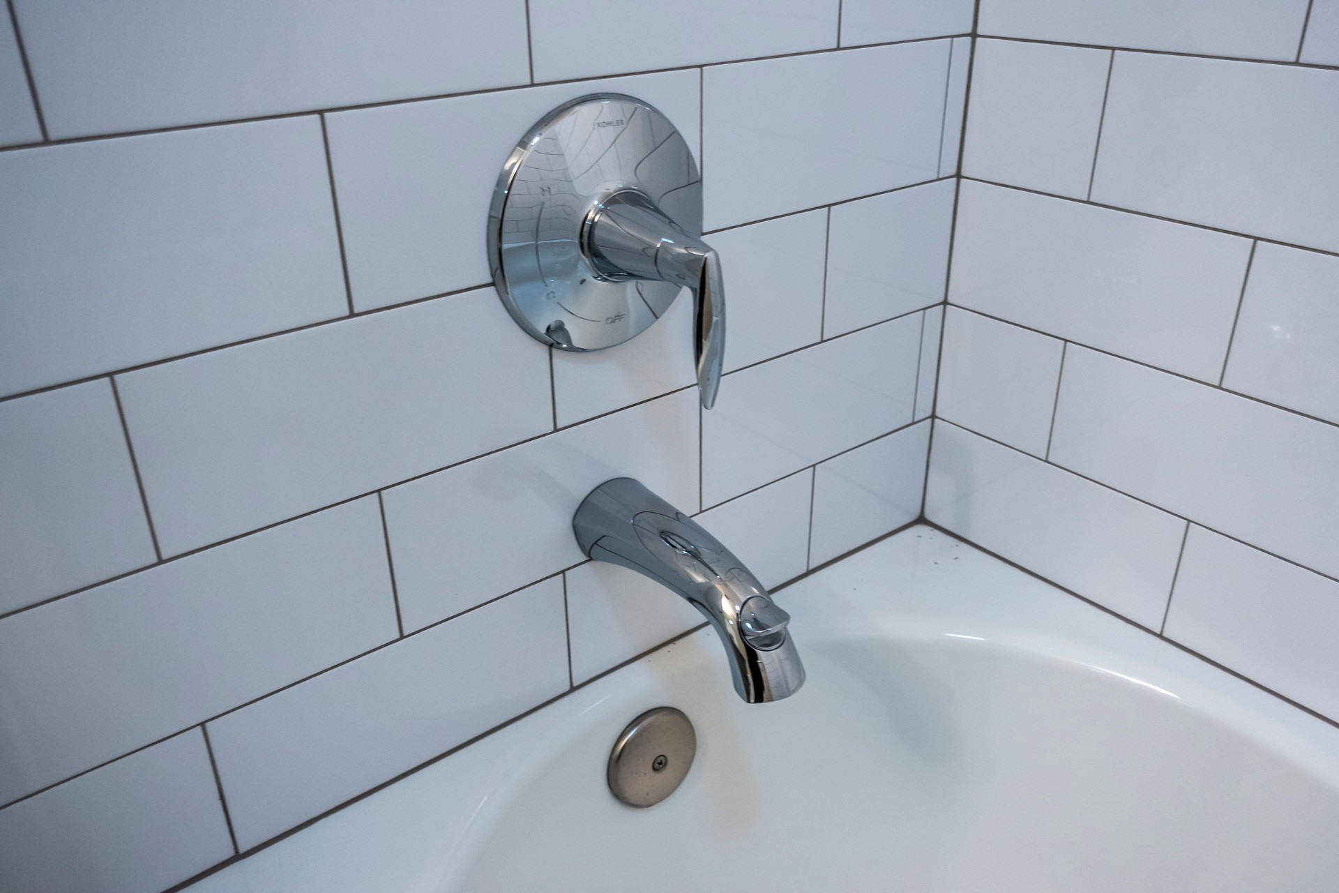 High angle view of a silver bath tub shower spout inside a white tiled bathroom