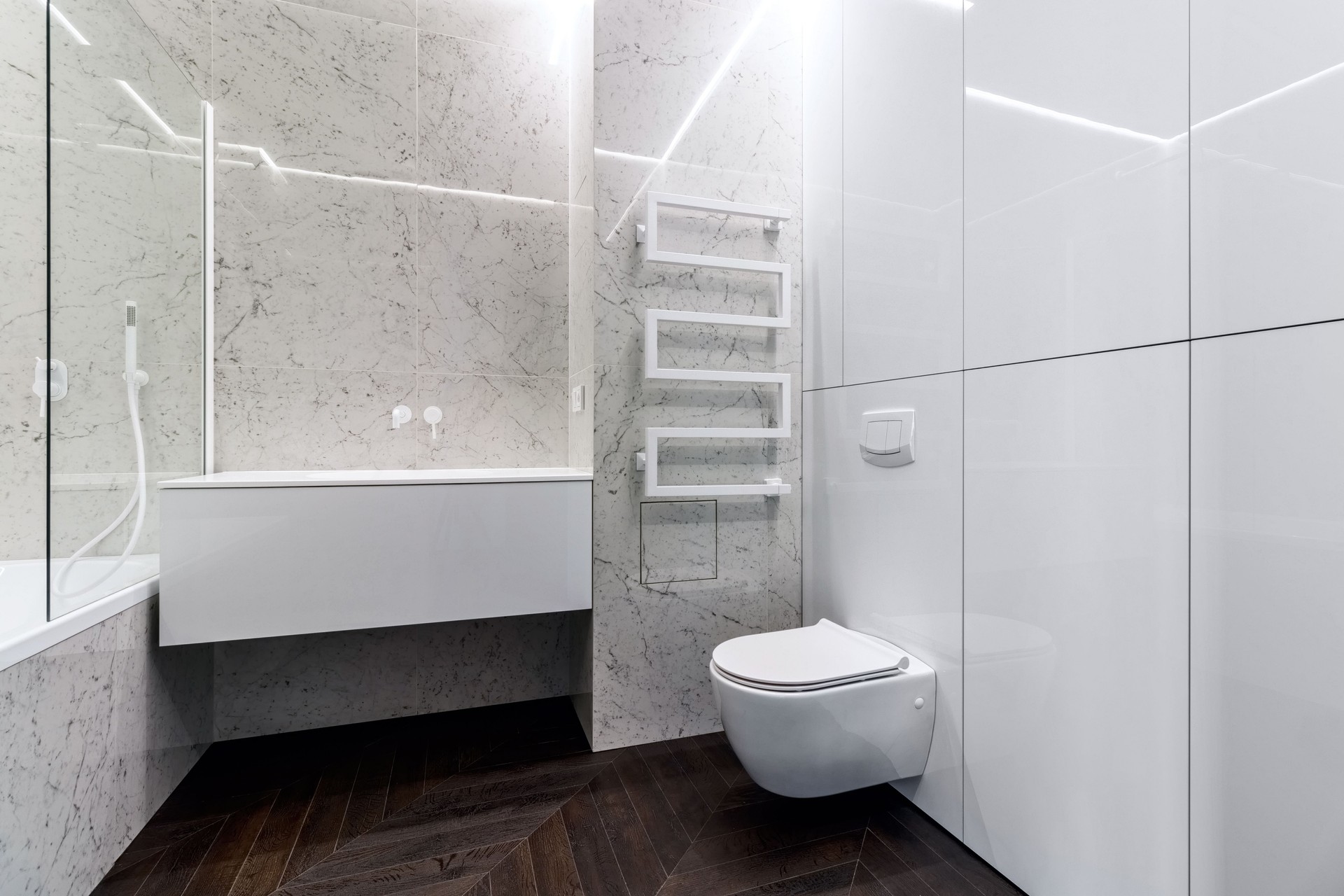 A luxurious interior in the bathroom with a bathroom, a shower on a shelf and a walk in the shower. White marble and dark brown floor. White cranes and plumbing