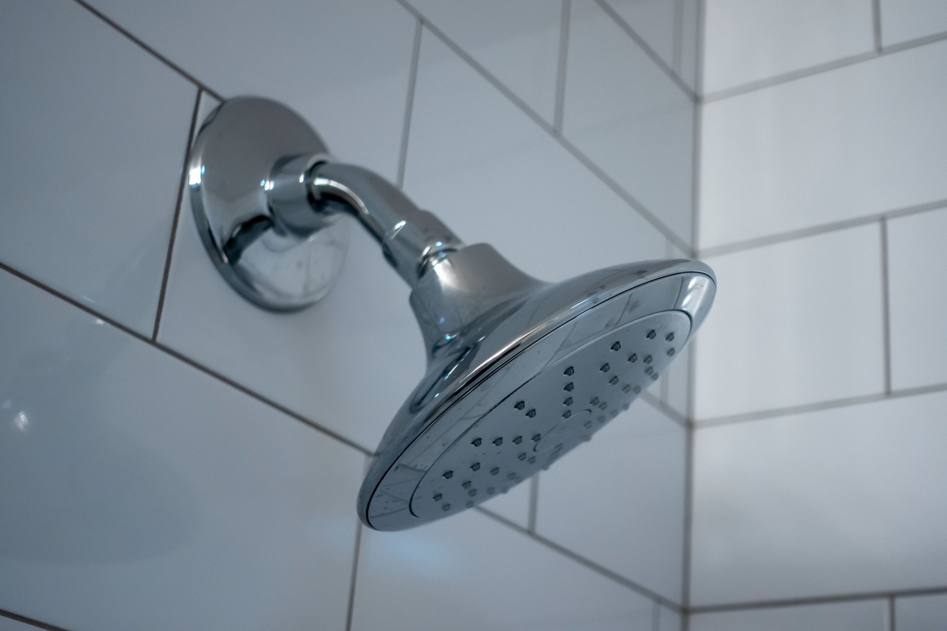 Selective, macro focus on a silver shower head inside a white tiled bathroom